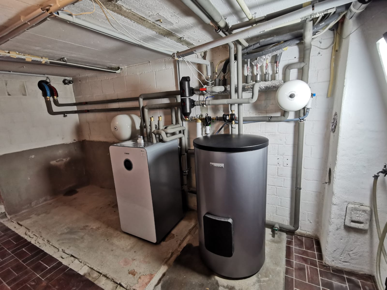 Wärmepumpen-Inneneinheit von Bosch mit Pufferspeicher, angeschlossen an ein komplexes Rohrsystem in einem sauberen Technikraum.